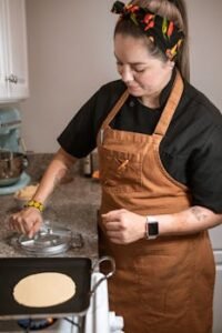 Female chef prepares tortillas with a tortilla press in a home kitchen, showcasing culinary skills.